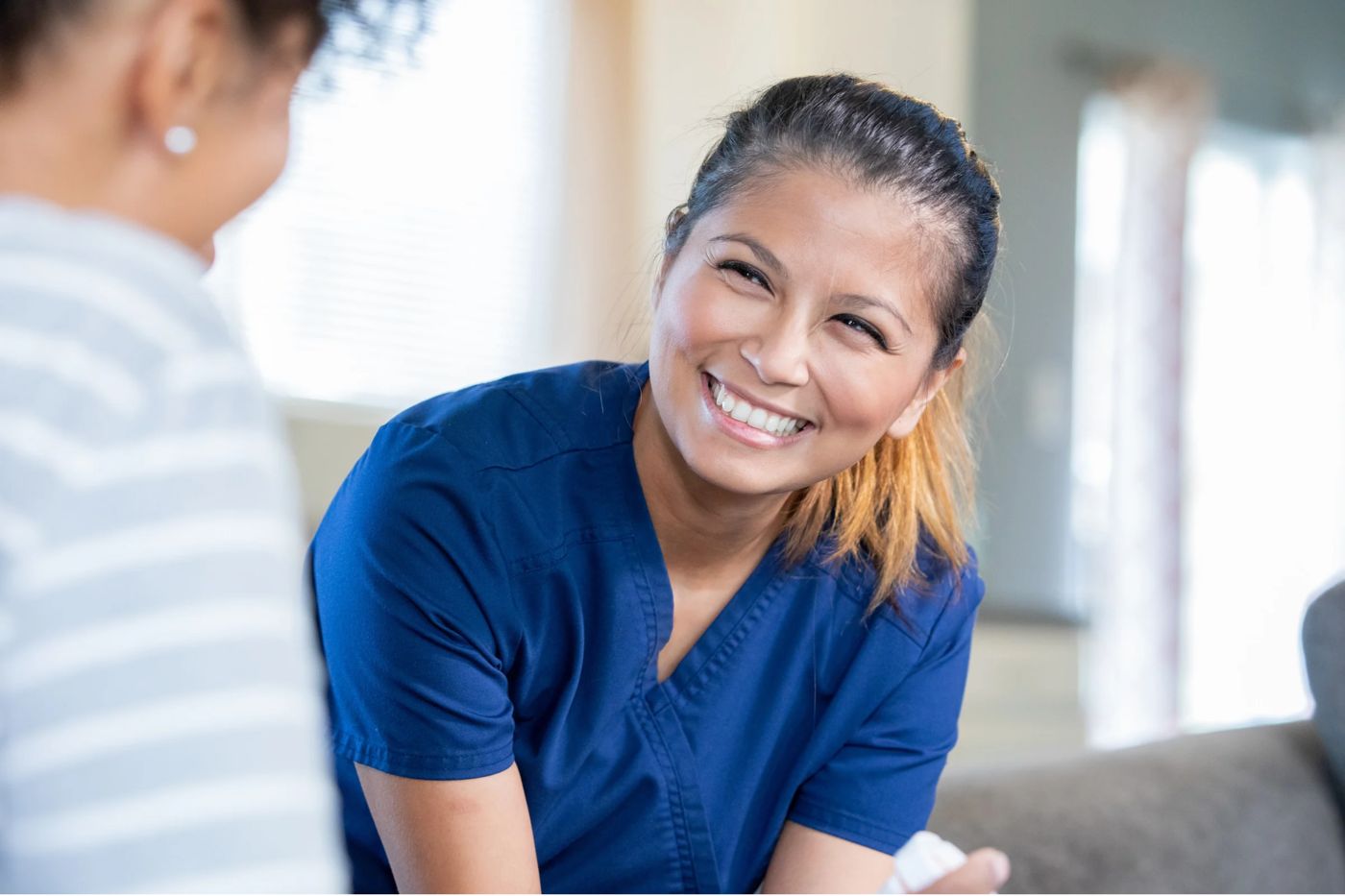 A smiling clinician in navy scrubs talking with a patient